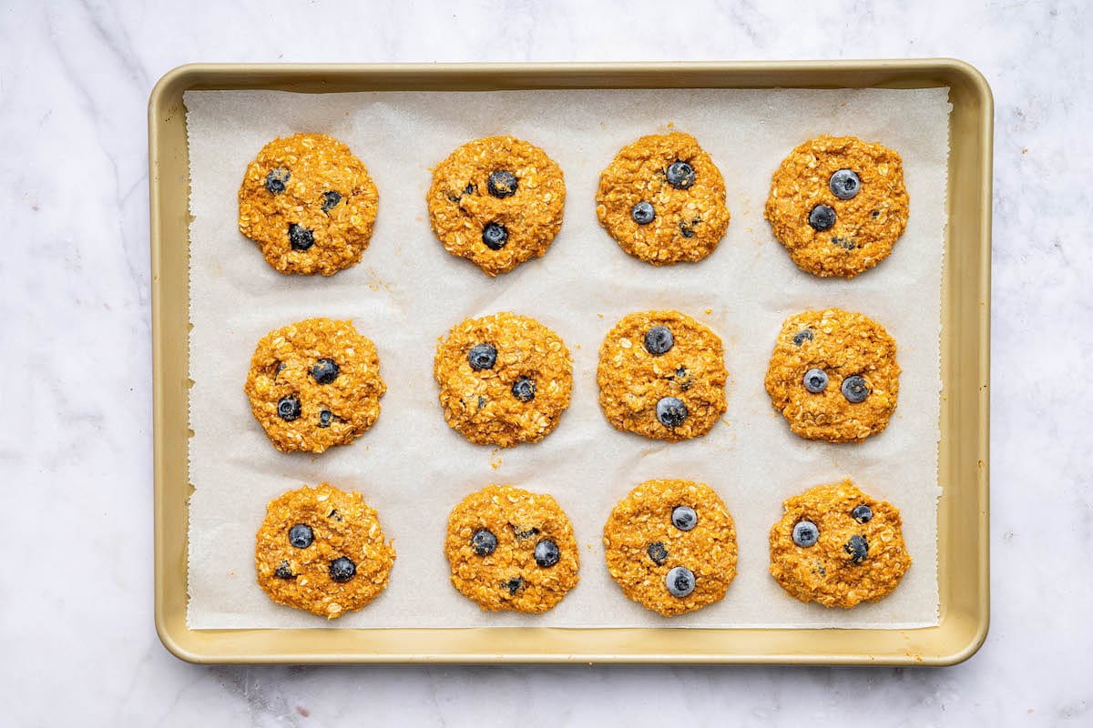 12 unbaked sweet potato blueberry oatmeal cookies on a baking sheet lined with parchment paper.