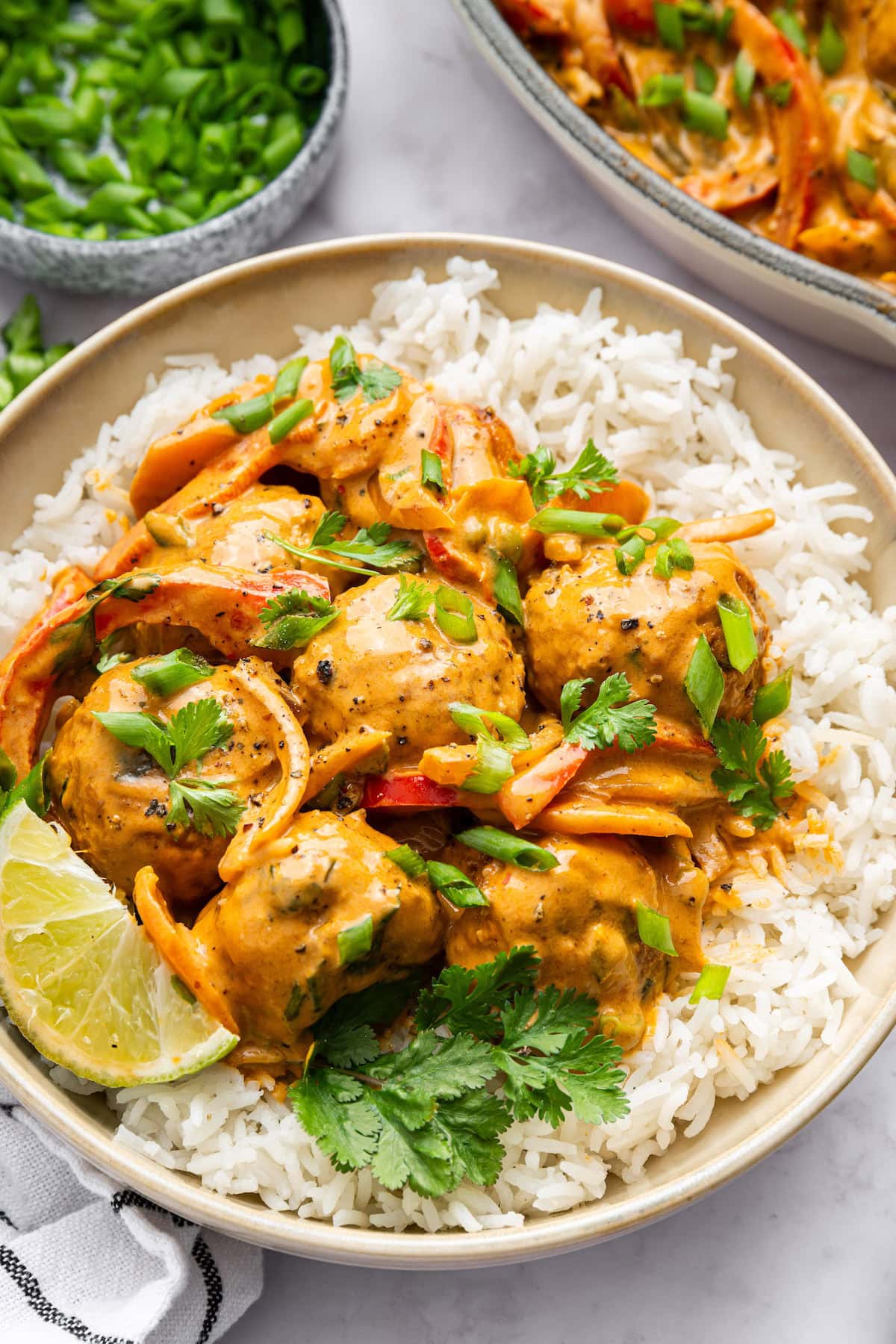 Thai chicken meatballs with coconut curry sauce and vegetables served over white rice. The meatballs are topped with green onion and cilantro.
