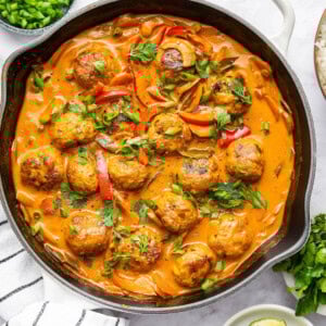 Thai chicken meatballs and vegetables simmering in a coconut curry sauce in a skillet. The meatballs are topped with fresh cilantro and green onions.