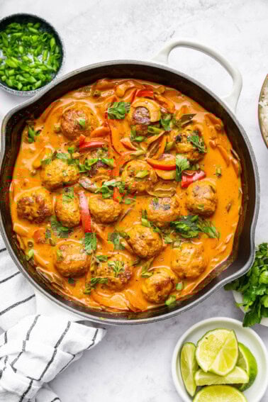 Thai chicken meatballs and vegetables simmering in a coconut curry sauce in a skillet. The meatballs are topped with fresh cilantro and green onions.