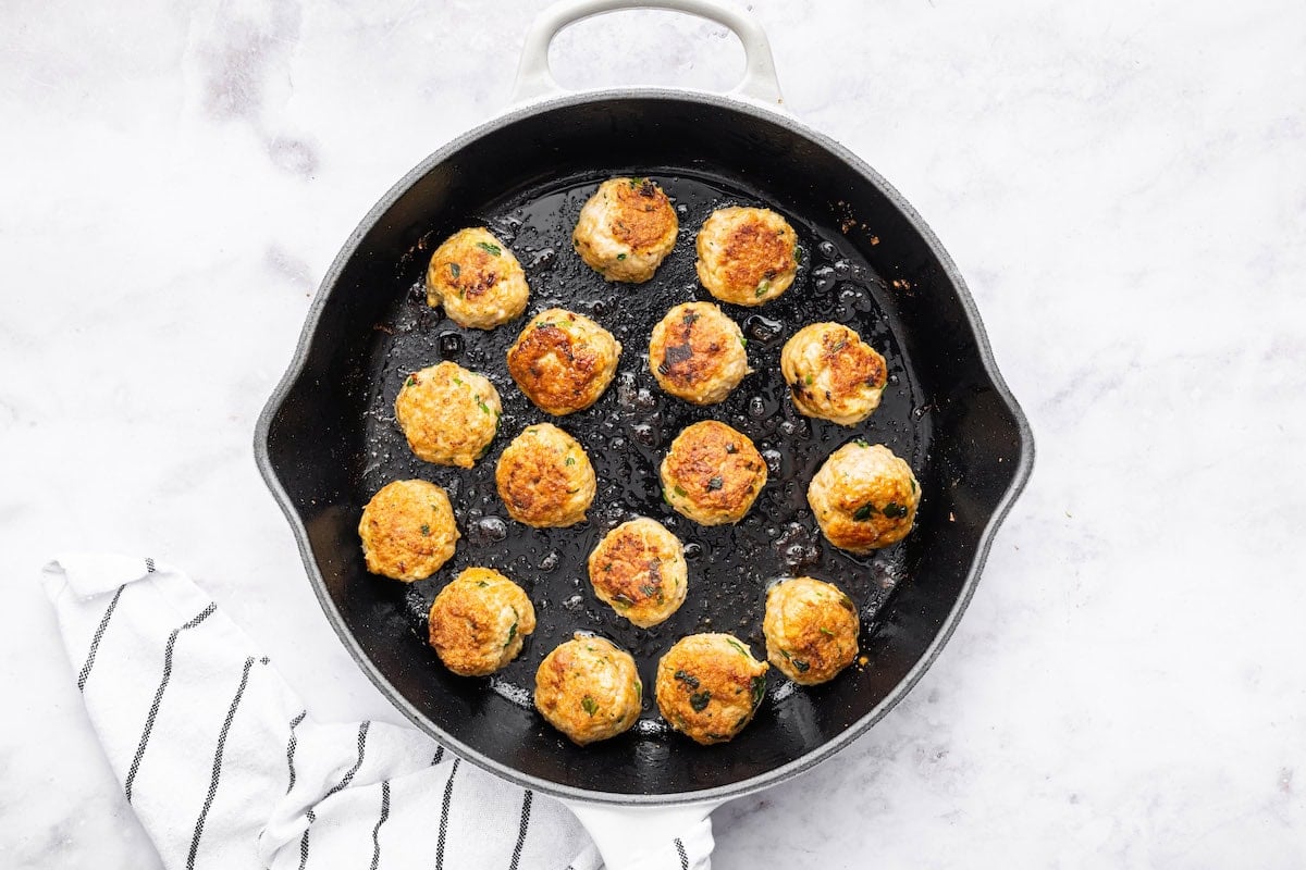 16 Thai chicken meatballs cooking in a skillet.