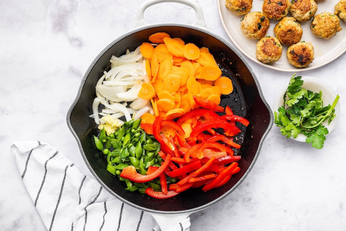 Vegetables for the Thai chicken meatballs in a skillet before being cooked: carrots, red bell pepper, yellow onion, green onion, garlic and ginger.