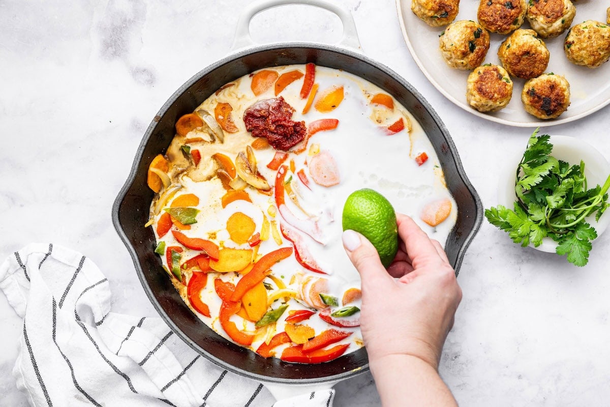A woman's hand squeezing lime juice into the coconut curry sauce for the Thai chicken meatballs.