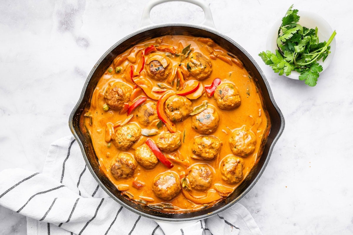 Thai chicken meatballs and veggies simmering in a coconut curry sauce in a skillet.