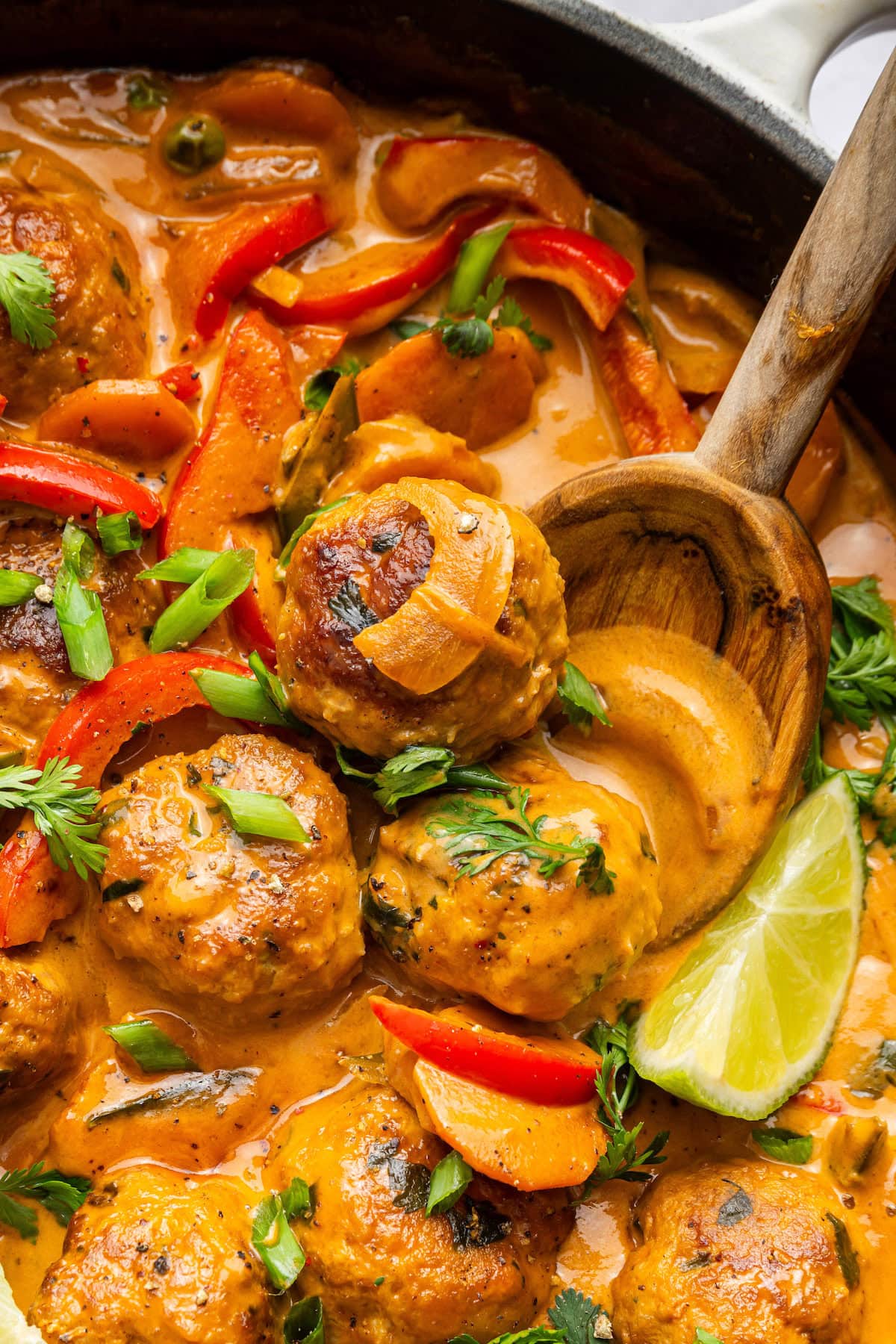 A wooden spoon scooping out three Thai chicken meatballs from the skillet.