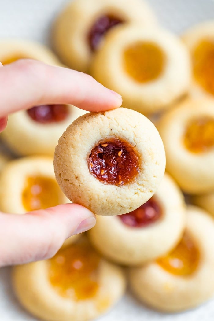 Almond flour thumbprint cookie with raspberry jam in a woman's hand.
