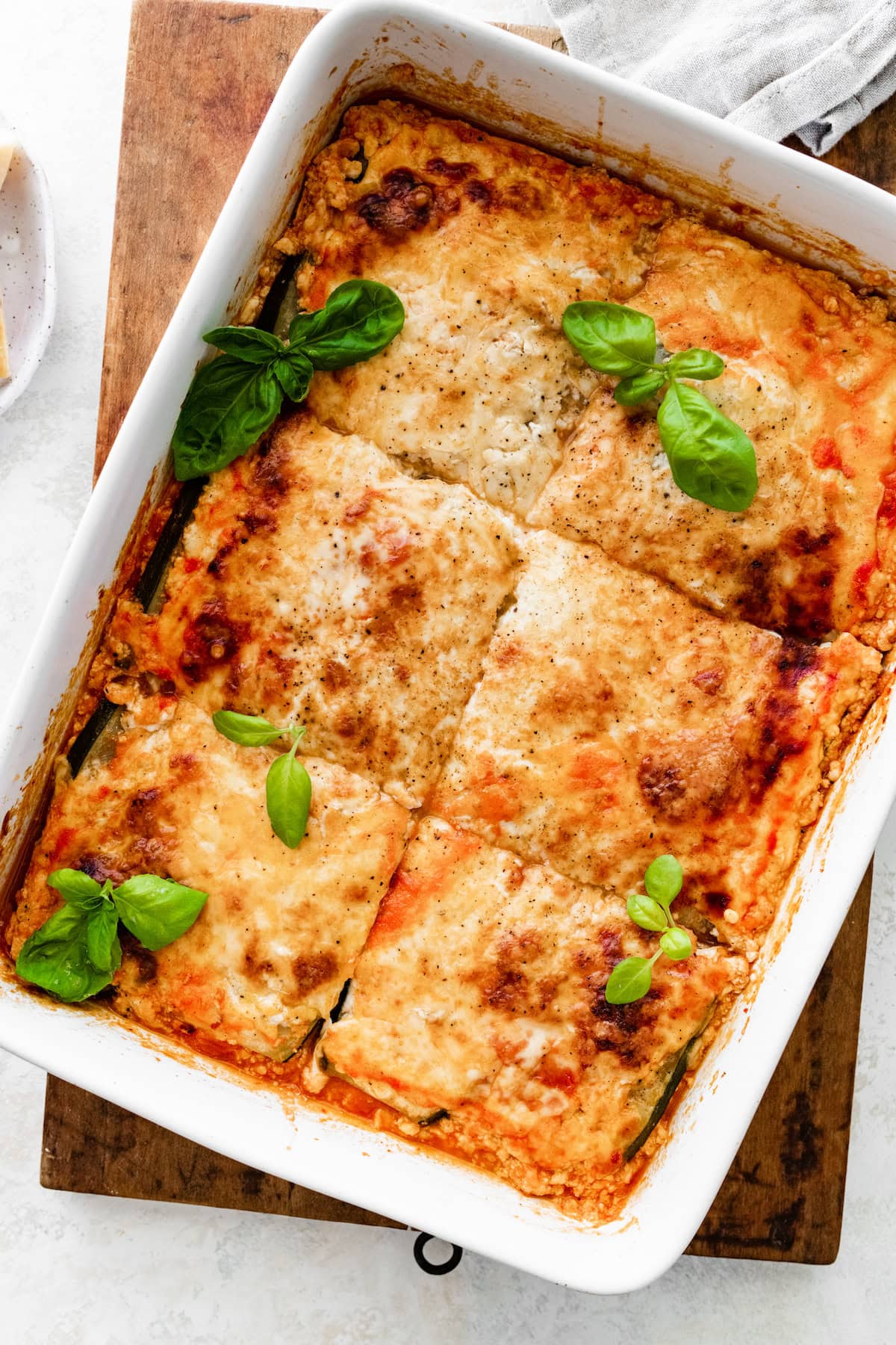 A square baking dish with tofu lasagna made with zucchini noodles cut into squares and garnished with fresh basil.