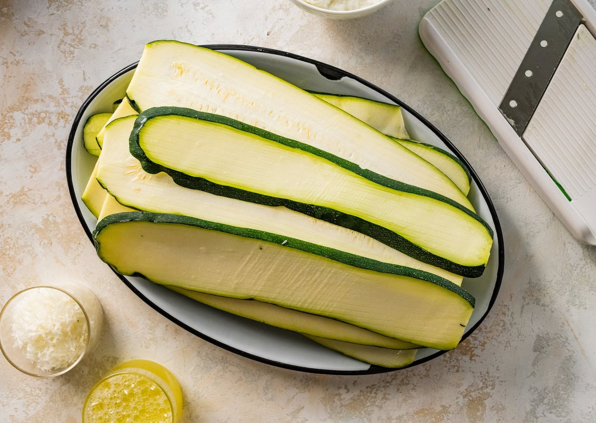 Multiple zucchini slices on a plate that will be used to make tofu zucchini lasagna.