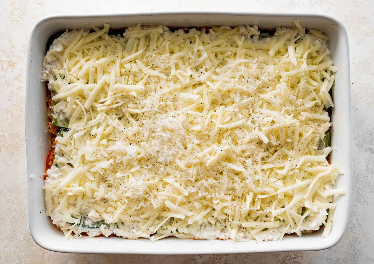 A layer of parmigiano reggiano and shredded mozzarella cheese to top off the tofu zucchini lasagana in a baking dish.