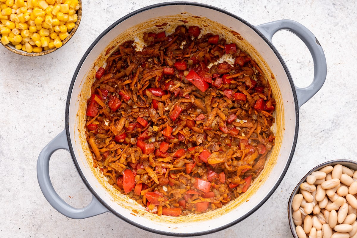 Cooked grated carrot, onion, and red bell pepper in a large pot.